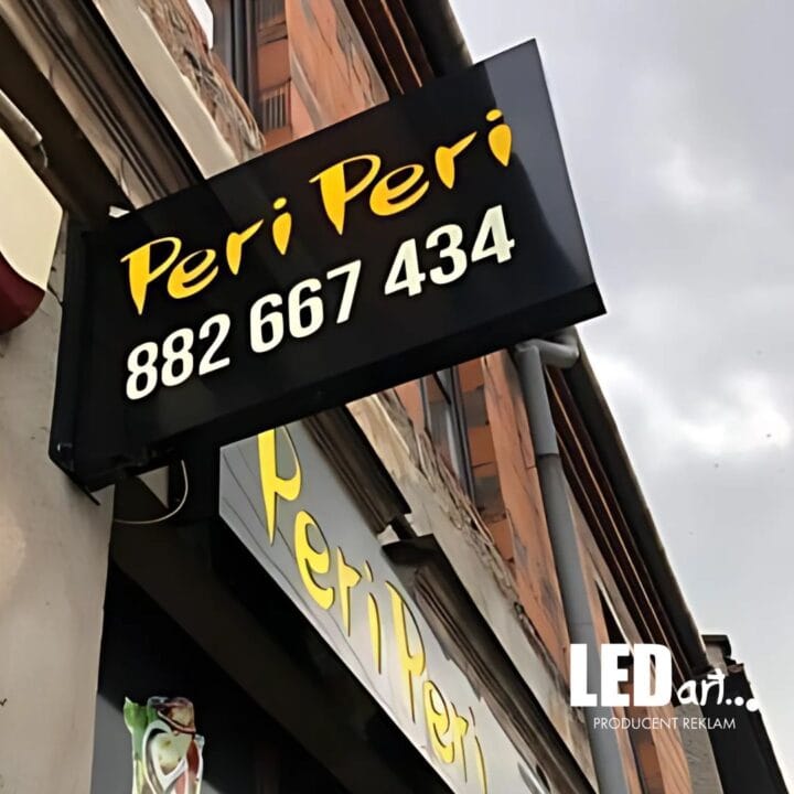 Dwustronny kaseton reklamowy na elewacji firmy PERI PERI, czarny dibond z białym logo.